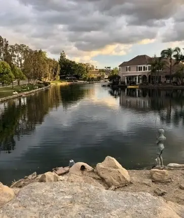 A lake with houses and rocks in the background.